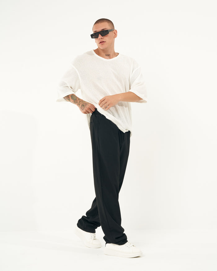 Martin Valen men's oversized black sports pants, mid shot of model adjusting waistband, visible side pocket