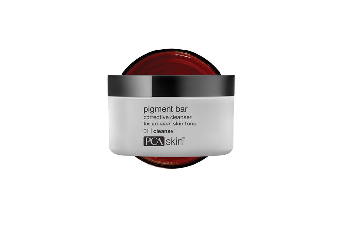 Pigment Bar | PCA Skin corrective cleanser in a white jar with a black lid, designed for an even skin tone, shown with the jar open revealing a deep red product inside.