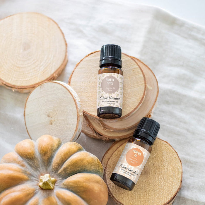 Two bottles of Eden's Garden essential oils on wooden slices with a pumpkin.