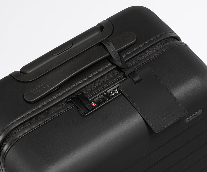 The Bigger Carry-On suitcase in Jet Black shown shown from above highlighting TSA-approved combination lock and recycled leather luggage tag
//
All of our suitcases come with a leather luggage tag. Add up to three letters to personalize yours and stand out at the baggage claim.