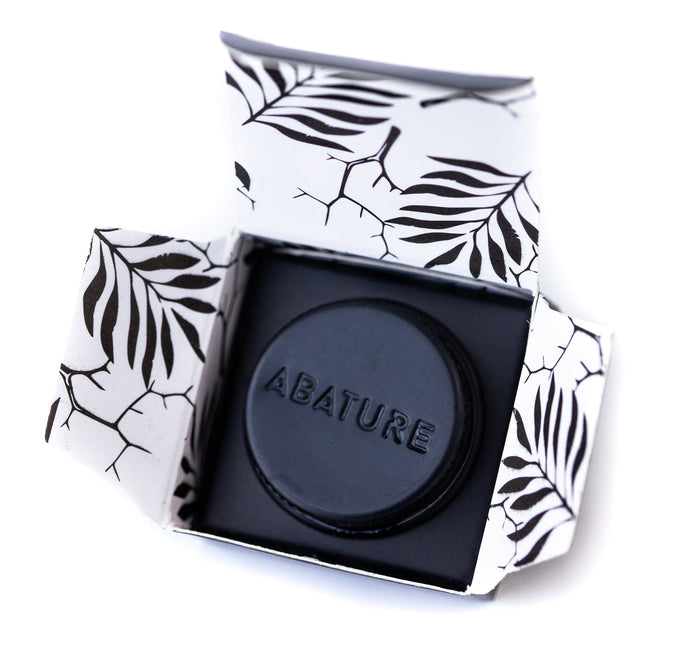 Black circular wellness device embossed with ABATURE, presented in an open box with a white and black leaf pattern, showcasing the Abature Mini | Abature for body care and recovery.