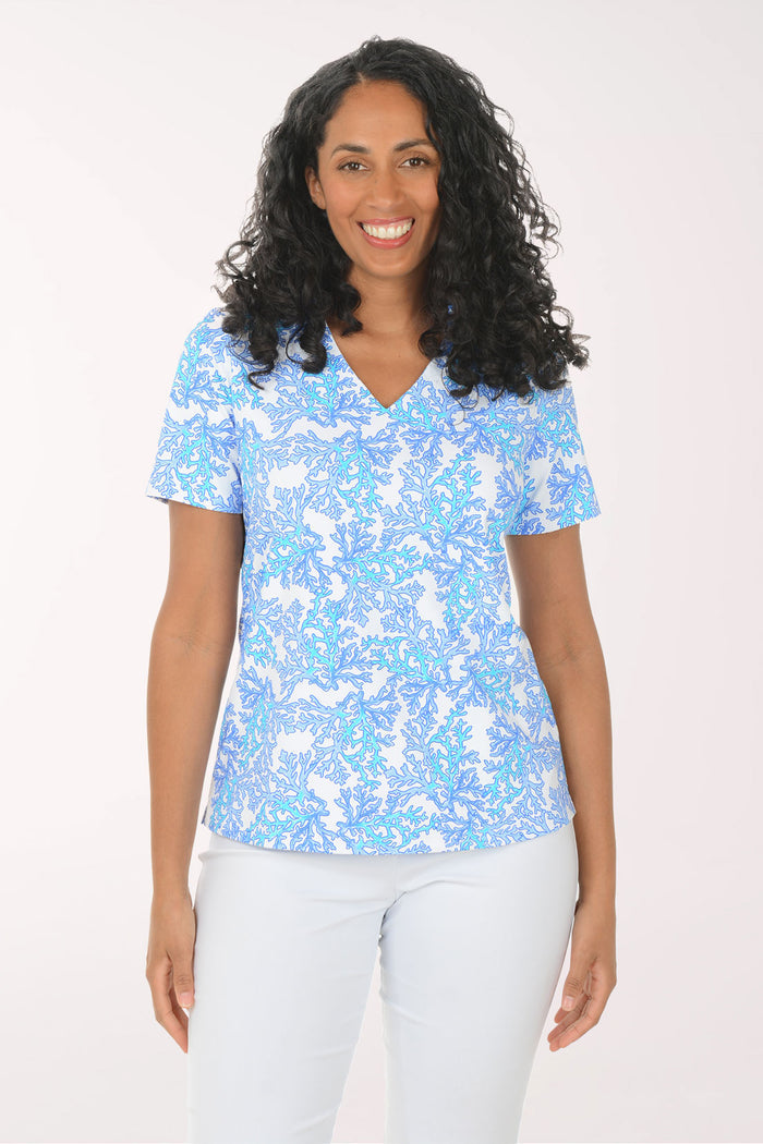 Woman wearing a blue patterned top and white pants on a white background