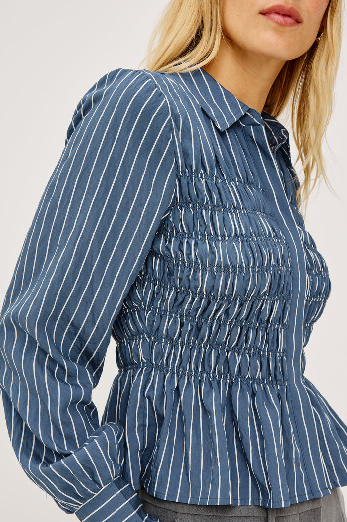Bradshaw Shirt in Cotton Poplin With Button-Up Front, Collar, Smocked Body, Peplum Hem, and Bishop Sleeves in Washed Indigo Stripe Colorway - Upper Body Side View Featured on Model