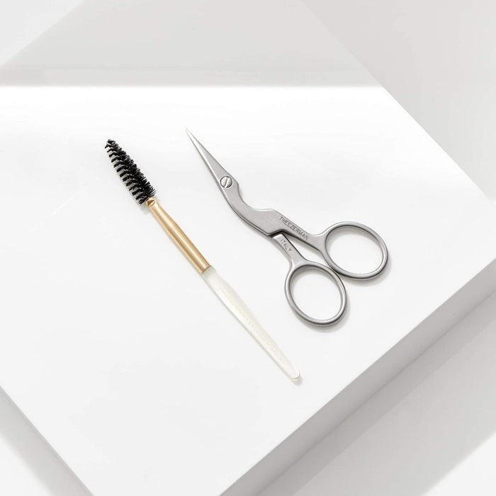 Brow Shaping Scissors & Brush | Tweezerman featuring sleek stainless steel scissors with curved blades and a spoolie brush with a white handle and gold ferrule for precise eyebrow grooming.