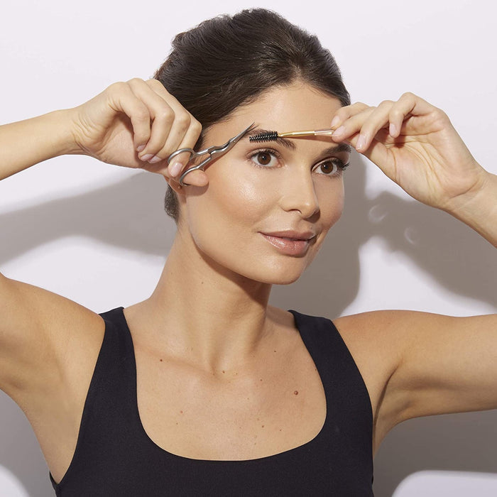 Woman using Brow Shaping Scissors & Brush | Tweezerman to groom and shape her eyebrows, demonstrating precise eyebrow care and maintenance.