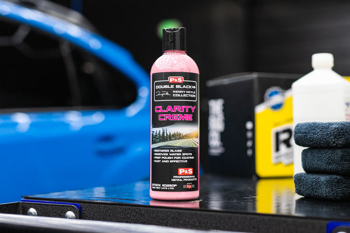Bottle of P&S Clarity Creme car care product on a workbench with a blue car in the background.