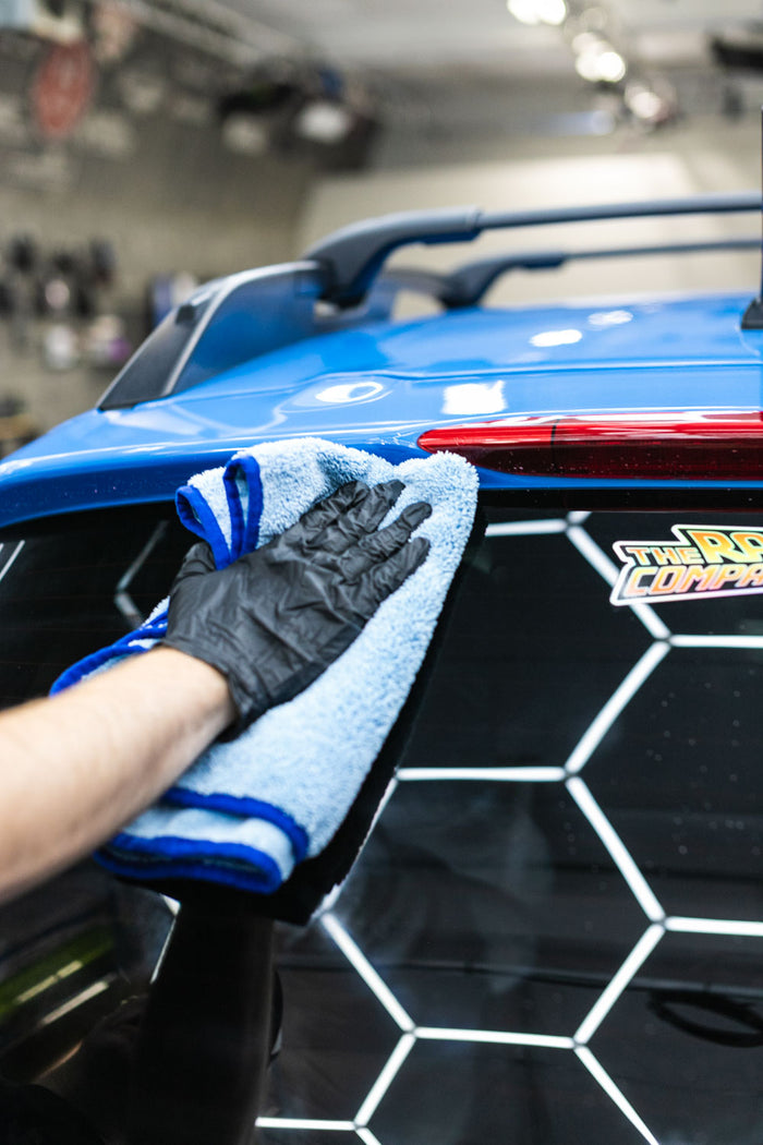 Person cleaning a car rear window with a blue microfiber cloth.
