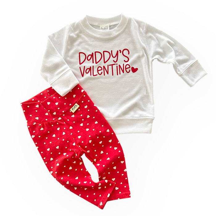 A handmade Valentine's Day outfit featuring a white pullover with the text "Daddy's Valentine" in bold red lettering, paired with red leggings adorned with small white hearts. The perfect festive set for your little one.