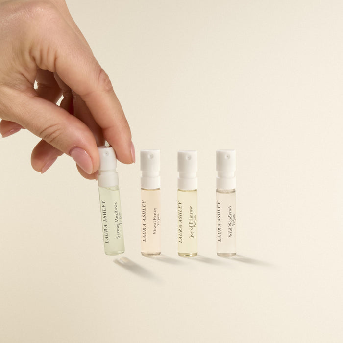 Hand holding a small bottle of Laura Ashley perfume with other bottles in the background on a beige background