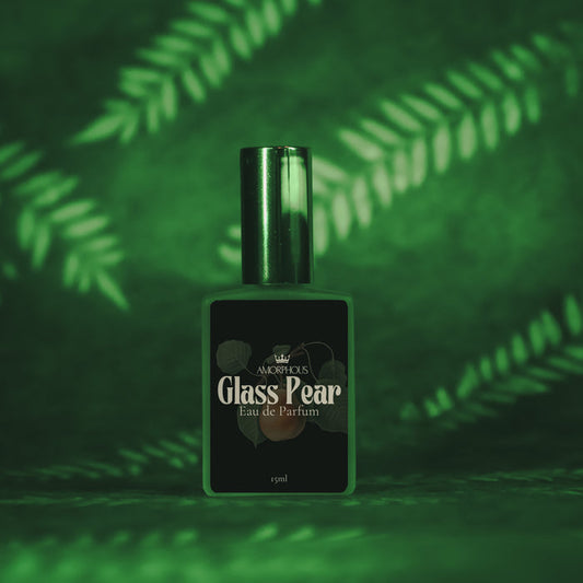 Green glass perfume bottle labeled 'Glass Pear' on a green leafy background