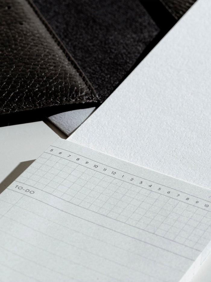Sticky note displayed with its backing next to a black leather agenda.