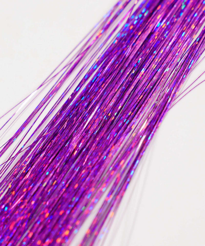 Close-up of several shiny Perfect Locks Perfect Hair Tinsel strands in Bubblegum, arranged diagonally on a white background. Reflective tinsel catches light with multicolored sparkles, resembling Remy hair extensions.#color_soft-purple