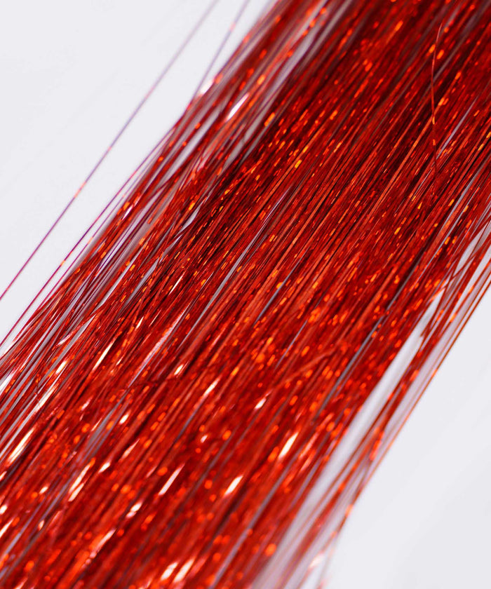 Close-up of many thin, shiny Hot Pink Perfect Hair Tinsel strands from Perfect Locks laid in parallel on a light background, resembling sparkling hair extensions as they reflect the light.#color_ruby-red