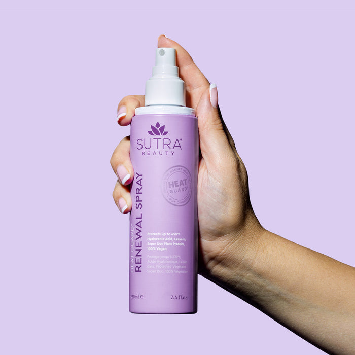 Hand holding a purple spray bottle of Heat Guard Renewal Spray | SUTRA against a lavender background, promoting skincare and beauty protection.