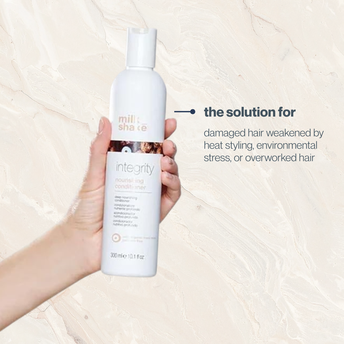 Hand holding a bottle of milk_shake integrity & strength hair product on a beige background
