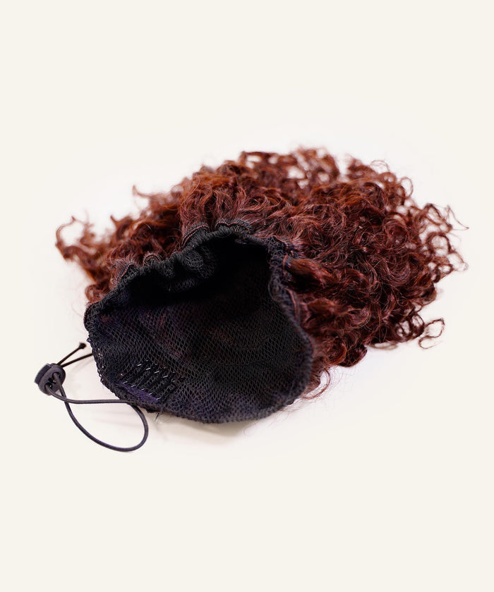 The Perfect Locks Kinky Curly Clip-In Bun in red has Remy hair extensions, a black mesh base, and adjustable drawstring on white.#color_burgundy-(99J)