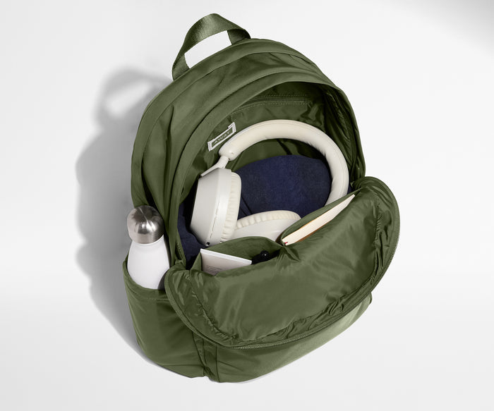 Green backpack with items like a bottle, mask, and headphones on a light gray background