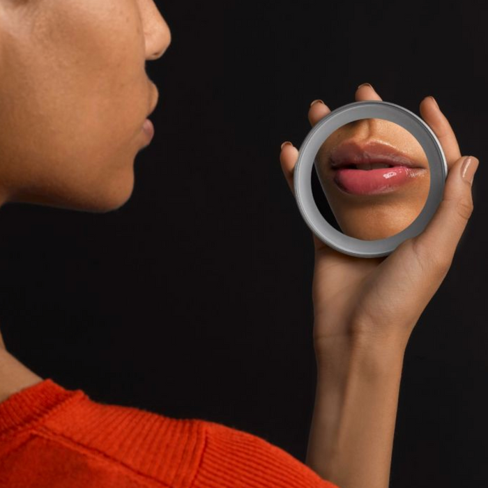 Person holding the LED 15X Lighted Mirror | Tweezerman close to their face, reflecting their lips with a focus on skincare and beauty detail.