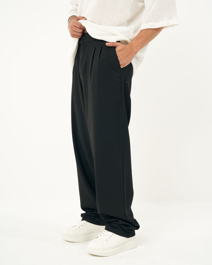 Martin Valen men's oversized loose-fit black sports pants, side close-up showing front pleats and hand placed in pocket