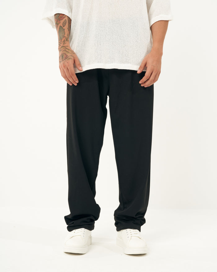 Martin Valen men's oversized loose-fit black sports pants, lower-body view with long hem partially covering white sneakers