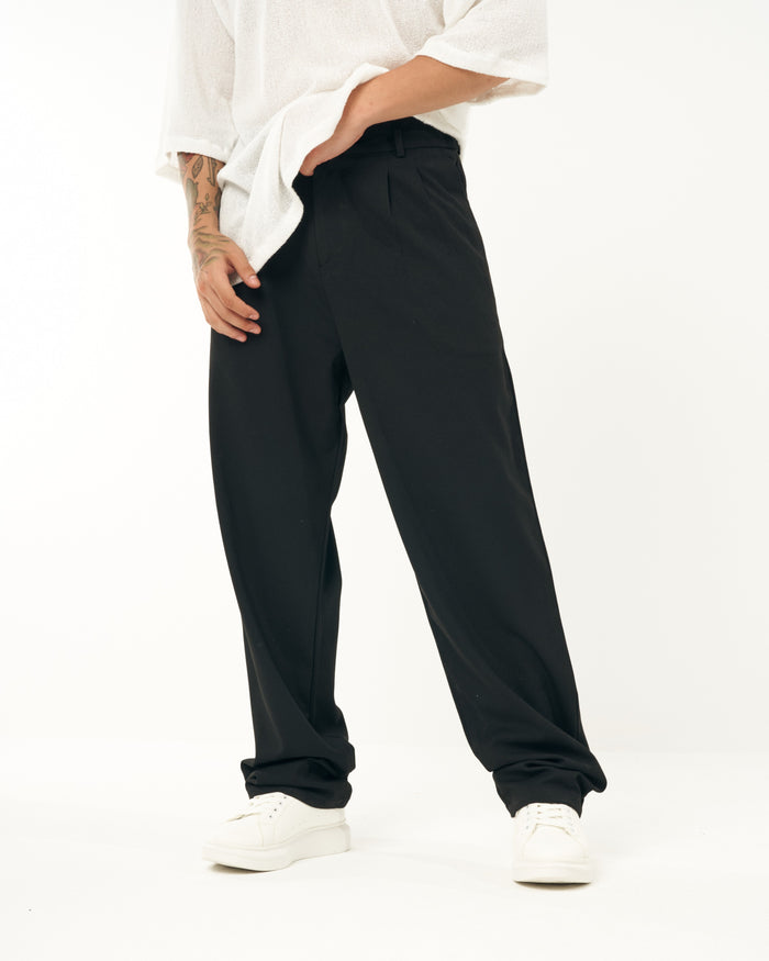 Martin Valen men's oversized black sports pants, close waist view showing pleat detail and model's hand in pocket