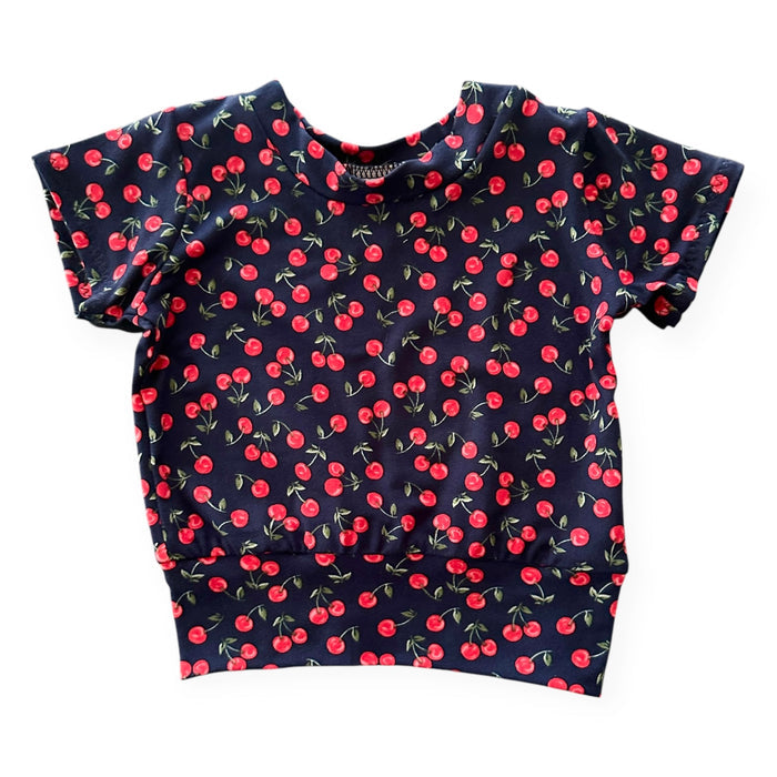 Midnight Cherries Baby T-Shirt – a short-sleeve handmade pullover with a cherry print on a navy background. Soft, stretchy, and perfect for stylish baby and toddler outfits.