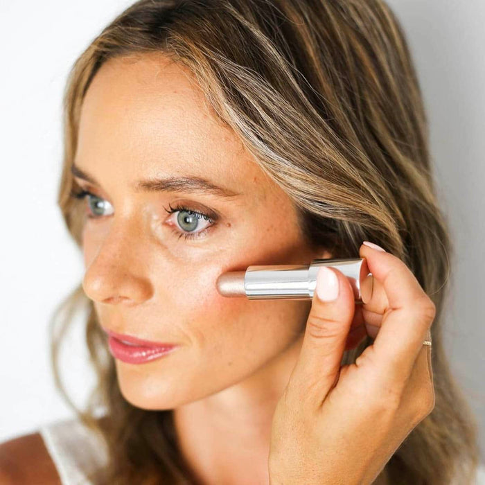 Woman applying cream highlighter to her face with a makeup brush.