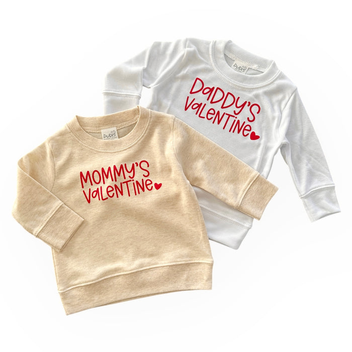 "Two baby and toddler sweatshirts with Valentine's Day designs, featuring Mommy's Valentine' in red on a neutral beige sweatshirt and 'Daddy's Valentine' in red on a white sweatshirt. Perfect for baby and toddler Valentine's Day outfits, showcasing cozy, handmade style.