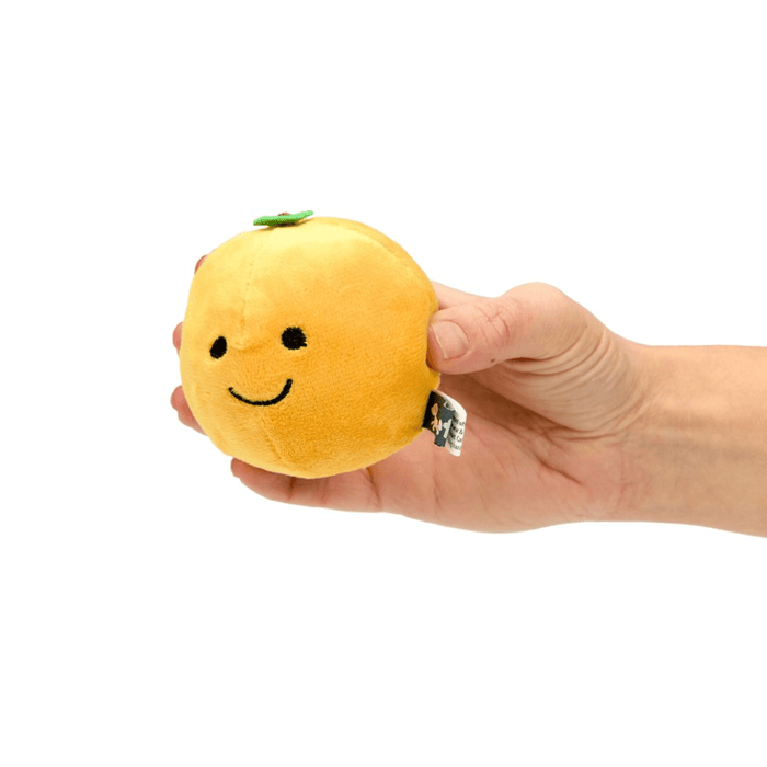 Orange fruit plush toy with green leaf detail and a smiley face in a person's hand.
