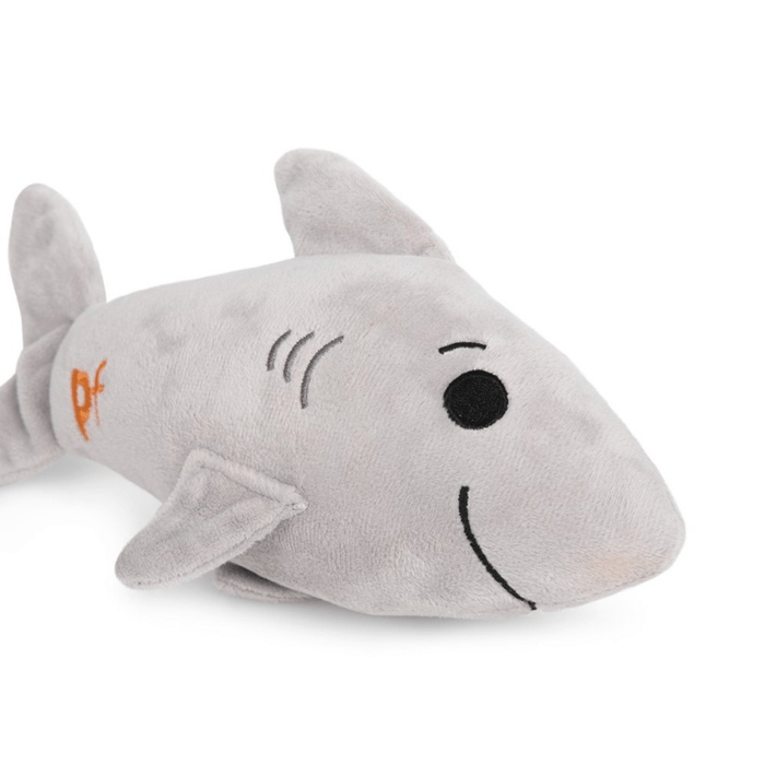 Close up view of grey plush toy shark with orange 'PF' detail on tail on white background.