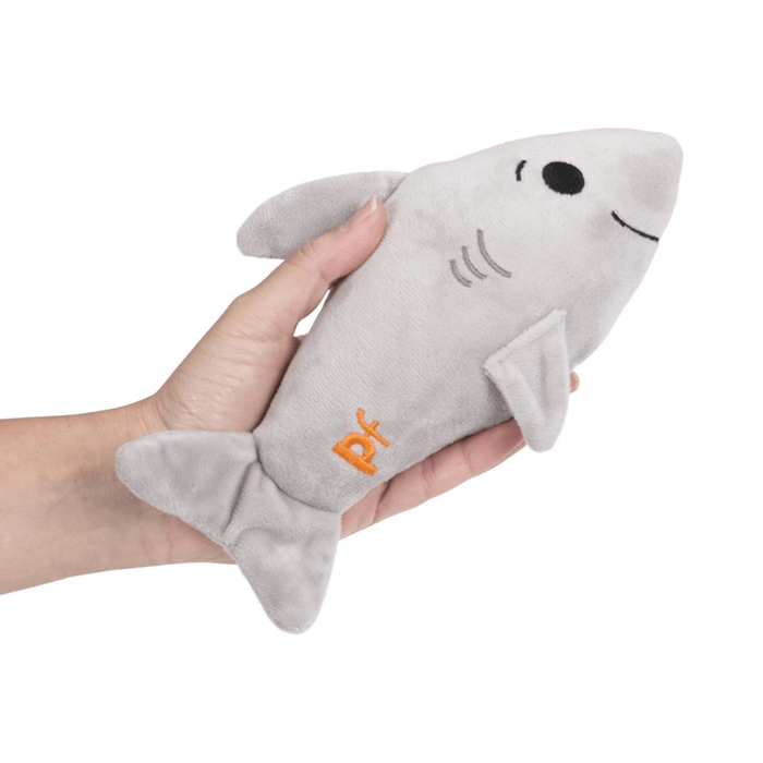 Hand holding grey plush shark toy with orange 'PF' detail on tail on white background.