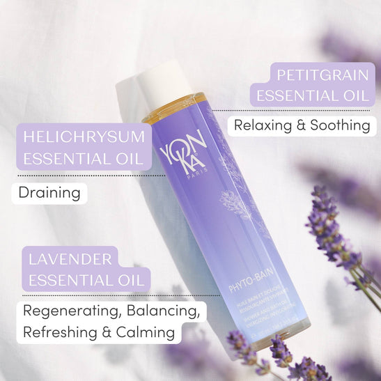 Bottle of Phyto Bain - Invigorating, Relaxing Aromatic Bath I Yon-Ka Paris surrounded by lavender flowers, highlighting ingredients heli­chrysum, petitgrain, and lavender essential oils with their benefits for skincare and relaxation.