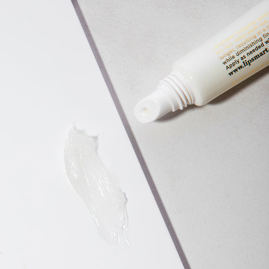 Close-up of a white tube dispensing clear balm onto a surface, showcasing the texture of PREMIUM LIP BALM | LipSmart in a clean, minimal skincare setting.