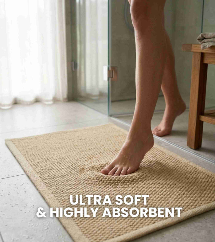 Beige bath mat on tile floor under bare foot, rectangular woven texture