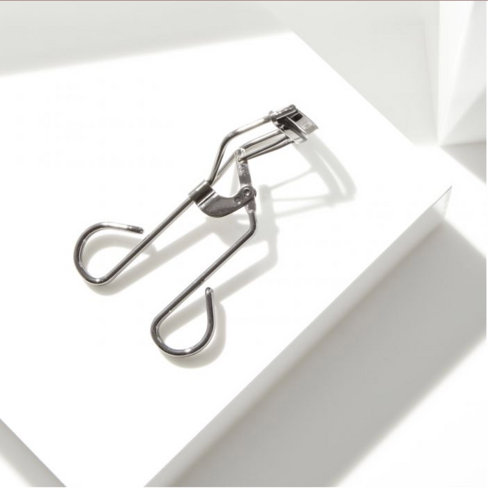 Pro Master Lash Curler | Tweezerman in stainless steel with a sleek design, shown on a clean white surface with soft natural light emphasizing its shape and details.