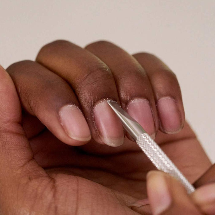 Close-up of a hand using the Pushy & Nail Cleaner | Tweezerman to gently clean under fingernails, showcasing precise nail care and grooming.