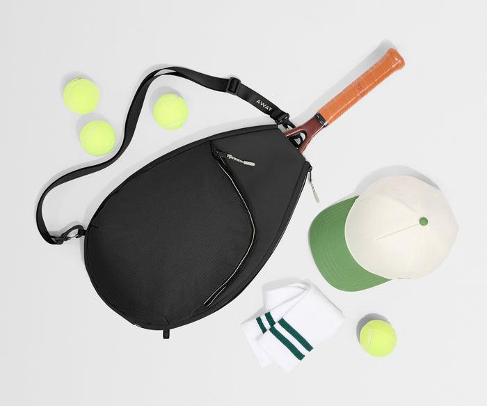 Black bag with a tennis racket, balls, and a cap on a light gray background