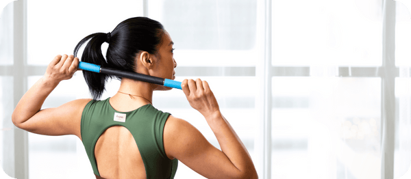 Person using Rod Mini | RAD in a teal color for muscle recovery and wellness, holding the device behind their back in a bright indoor space.