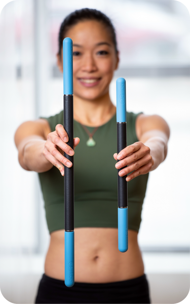 A woman in athletic wear holding two blue and black Rod Mini | RAD recovery tools, demonstrating the difference in size between the standard and mini versions.