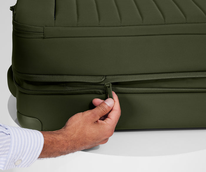 A person is unzipping The Softside Bigger Carry-On suitcase in Olive Green using the wraparound zipper to access 1.75" (4.5 cm) of extra packing space
//
An additional wraparound zipper allows you to expand the Softside suitcase easily when you need extra room.