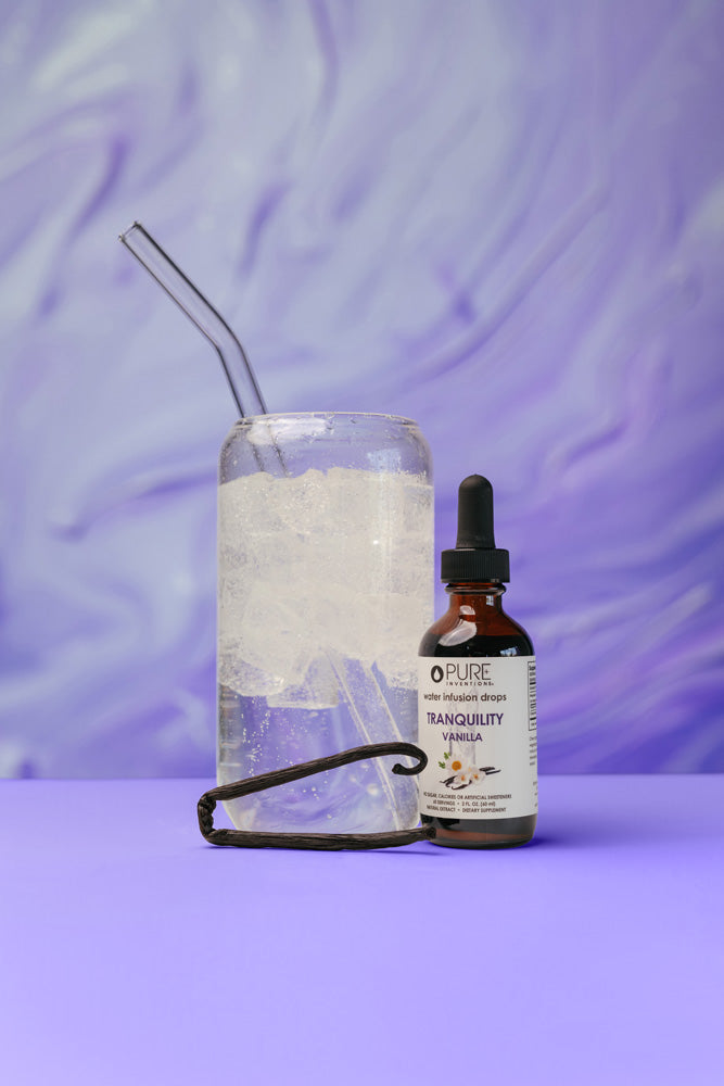 Tranquility Vanilla Water Infusion Drops | Pure Inventions bottle next to a glass of iced water with a straw and a vanilla bean pod on a purple surface with a soft purple background, promoting wellness and hydration.