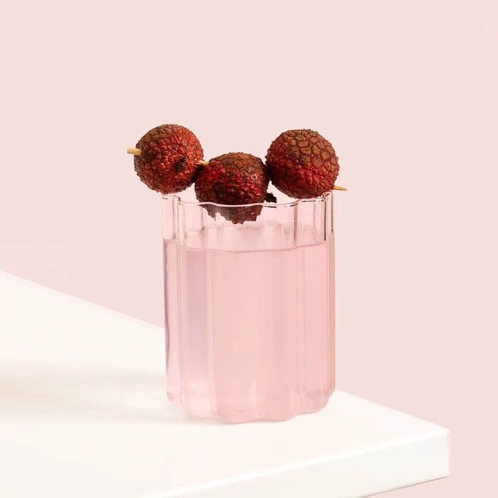 Stylish wavy glass of light pink protein water with lychees on a pink background.