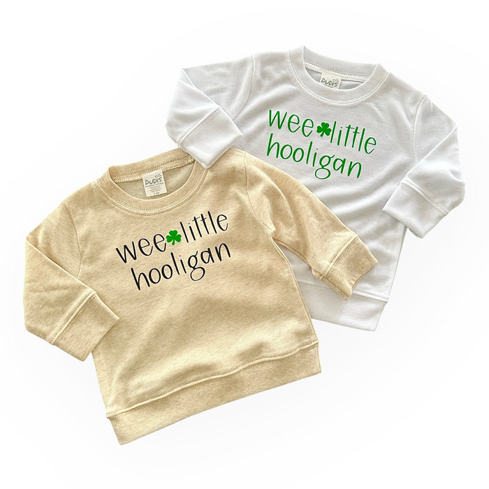 Handmade 'Wee Little Hooligan' pullover for babies and toddlers, featuring a fun St. Patrick's Day design with a shamrock. Soft, cozy, and perfect for celebrating in style. Available in beige and white options.