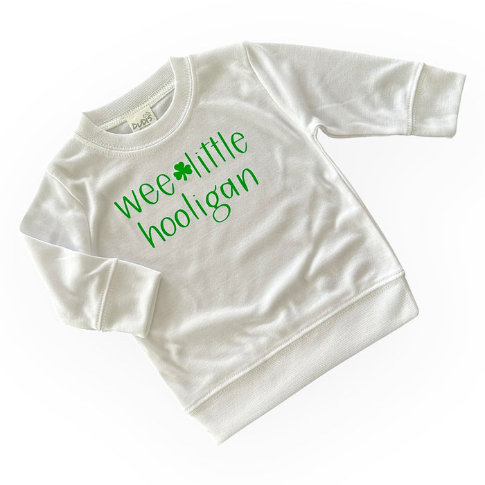 White 'Wee Little Hooligan' pullover for babies and toddlers, featuring a playful green shamrock design. Perfect for St. Patrick's Day celebrations or everyday wear. Soft, cozy, and made for little ones with comfort in mind.
